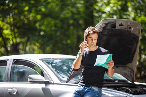 Man standing outside his damaged vehicle looking over his insurance policy in FL, NC.