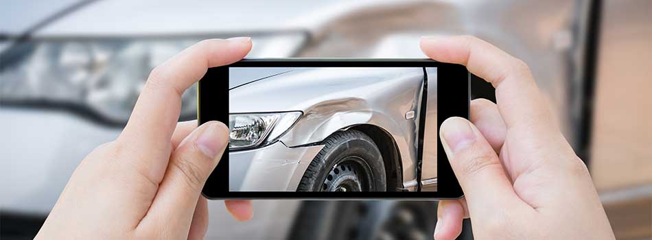 Auto insurance adjuster taking a picture of a damaged car after an accident.